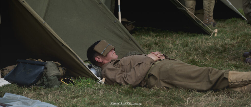 A serene scene of a WWII US soldier lying in the grass, taking a nap in front of a tent. The soldier appears relaxed and at ease, embodying a rare moment of calm amidst the chaos of war.
